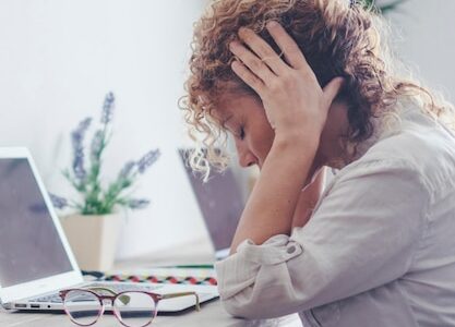 Uma jovem caucasiana indisposta trabalha no computador no escritório em casa tira os óculos sofre de enxaqueca ou dor de cabeça Infeliz cansada mulher milenar luta com tontura ou visão embaçada usando laptop